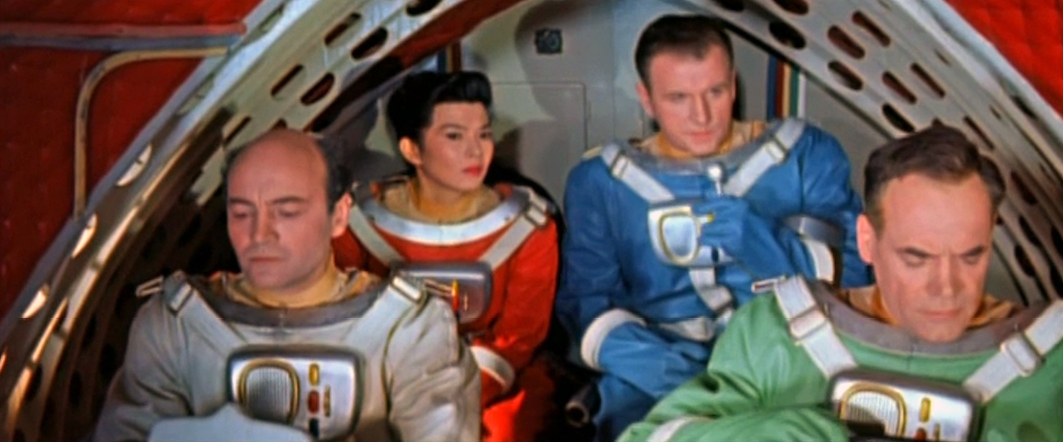 A still from the 1960 East German science fiction film ‘The Silent Star’ (Schweigende Stern), depicting astronauts in red, blue, and teal space suits in a space environment. The colorful suits reflect the retro-futuristic aesthetic.”,