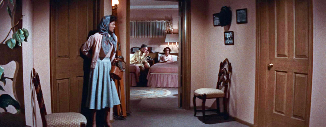 A hallway scene from “”Rebel Without a Cause”” where a young woman cautiously stands in the foreground, peering into a bedroom where two people are engaged in conversation. The lighting and composition create a tense and introspective mood.”,
