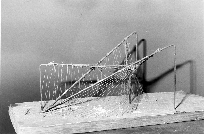A black and white image of a string model of Xenakis’s design for the Philips Pavilion. The delicate structure consists of thin wire and numerous strings intricately arranged to demonstrate the geometric properties and force distribution in the bridge design.”