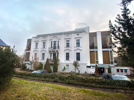 Photograph of grand, three storey house with eighteenth century white stucco façade and balconies, flanked by contemporary glass and steel extensions.