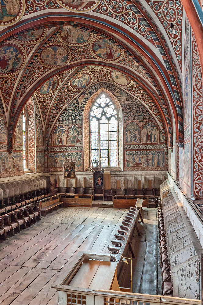 The view of the nuns’ choir shows the last two bays, painted with scenes from the life of Christ on the ceiling, and from the Old Testament and saints’ lives on the west wall. At the centre of the west wall, below a large Gothic window, is the throne for the abbess; on either side of this are the choir stalls for the nuns running in two rows along the north and south sides, with an elevated floor for the back row under which hundreds of small objects were found; the front rows start with a lower bench for the younger girls in the convent.