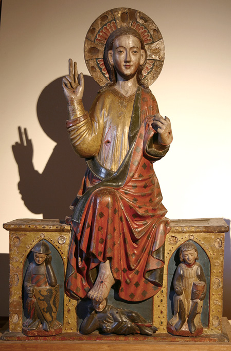The wooden sculpture shows the figure of Christ rising from his tomb. He wears a gold tunic, slit open to expose the wound in his side surrounded by red and with a hole drilled through it. Over his left shoulder is draped a red toga, under which his right foot is visible. On the side of the tomb are carved the figures of three sleeping knights. Most of the precious stones which decorated the halo and the tomb are lost but the places where they were attached are still visible. At Christ’s side is empty space which would have been filled by two angels. For a full description of the staging of the figure see Chapter IV.3.