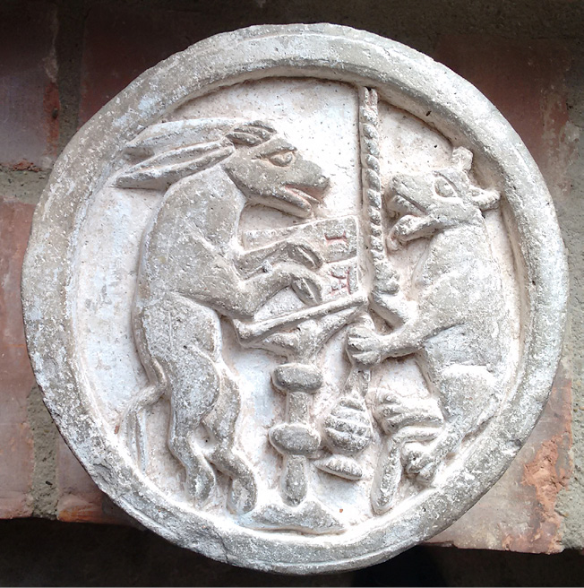 In its round medallion the former keystone from the cloisters of Kloster Ebstorf, which has now been taken down, features a donkey standing on its hind legs, with its front hoofs placed below the letters ‘I’ and ‘A’ in a large book on a lectern. Opposite him is a wolf, also on its hind legs; its right paw holds a candle, or pulls a bell with it, and its left paw holds a censer. See description in Chapter IV.2.