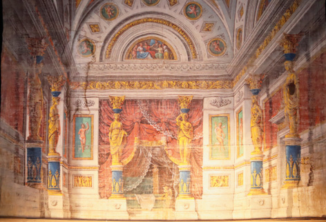 Romolo Liverani, Cabinet (« gabinetto ») Fond de scène peint sur toile représentant une scène de cabinet. La pièce est construite sur un plan rectangulaire. La paroi du fond représente une alcôve dans laquelle se trouve un lit à l’Antique, caché par des draperies rouges et transparentes. L’alcôve est encadrée par deux cariatides dorées soutenant un entablement coiffé d’un tympan décoré de tables rappelant des peintures de style pompéien. Les parois latérales de l’espaces sont décorées de la même manière, avec cariatides et tables représentant des peintures de style pompéien.
