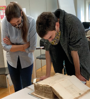 Une photographie présentant un étudiant et une étudiante consultant un épais registre de l’Académie de Lausanne datant du XVIe siècle, conservé aux Archives Cantonales Vaudoises.