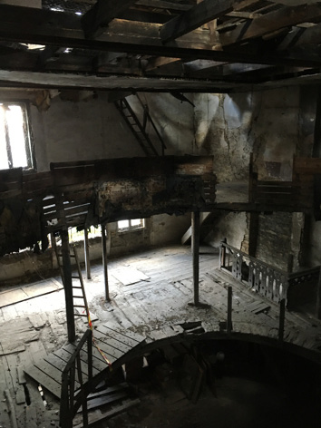 La photographie montre l’intérieur d’un théâtre délabré par le temps – que nous appellerons le « Vieux Théâtre » –, avec ses balcons en bois abîmés dans un état de ruine avancée. Le point de vue regarde vers le fond de la salle.