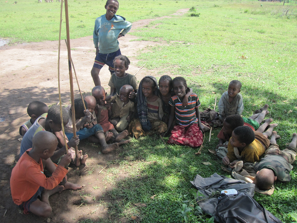 Photograph of Guji children sitting on the grass in a cattle herding field and engaged in a storytelling session