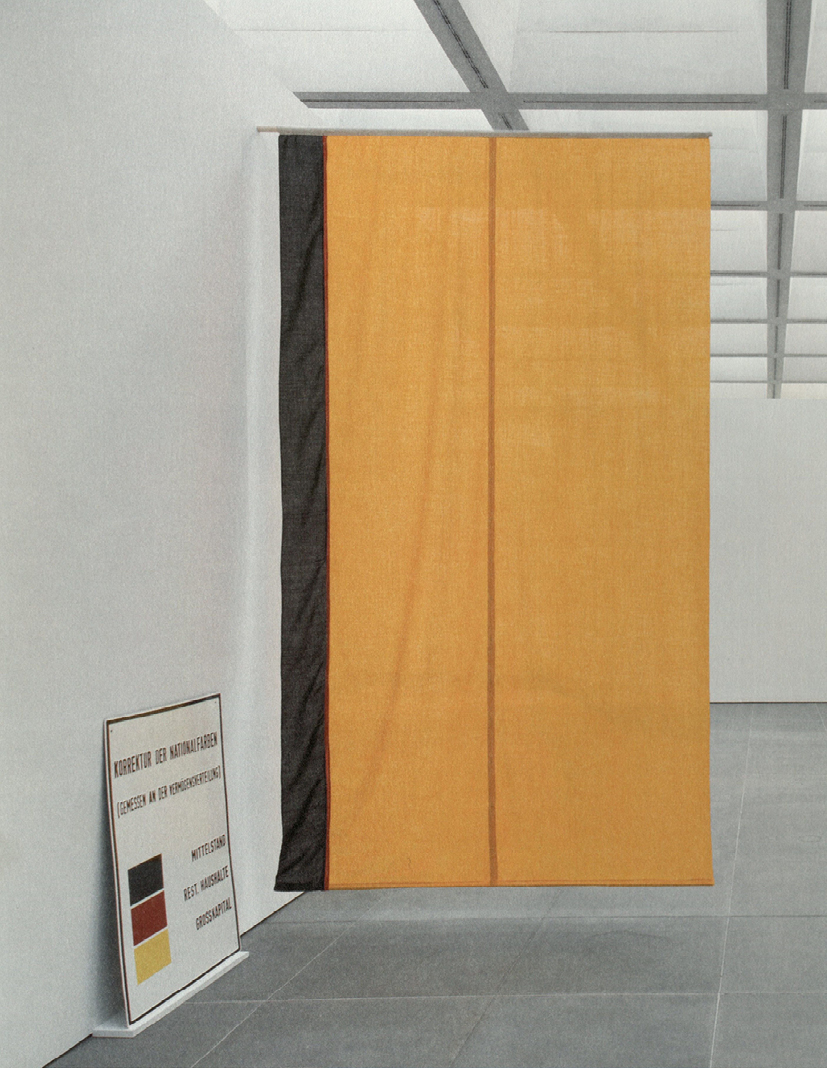 An art installation by German artist K. P. Brehmer from 1972, displaying a reimagined West German flag. The hanging fabric is divided into three vertical sections: a large orange-gold panel on the right, a narrow black strip on the left, an almost invisible band of red. In the bottom left corner, leaning against the wall, is a chart or diagram that explains the concept, showing the three flag colors and accompanying German text.