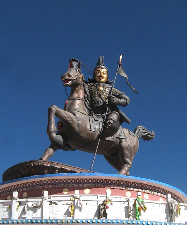 A large statue of a warrior wearing traditional armour and holding a flag, mounted on a galloping horse. The statue is positioned on a decorated pedestal with white and gold detailing, and the deep blue sky forms a contrasting backdrop.