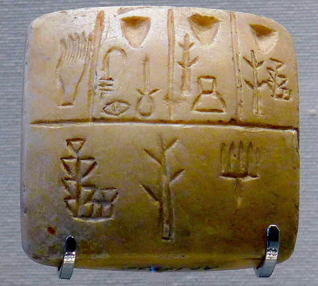 A close-up of an ancient Sumerian clay tablet with early cuneiform inscriptions. The carvings show pictographic symbols representing objects or concepts, likely an early form of record-keeping.