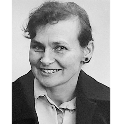 A black and white portrait of a middle-aged woman with short wavy hair, wearing a collared shirt and a dark coat. She has a warm, gentle smile and expressive eyes, conveying a friendly and approachable demeanour.