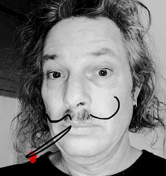 A digitally altered black and white photograph of a man with curly, unkempt hair, with an added cartoonish moustache and a drawn cigarette. His wide-eyed expression and messy hair give him a humorous and eccentric appearance.